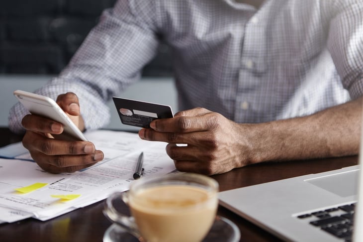 Man's hand holding credit card while working at computer