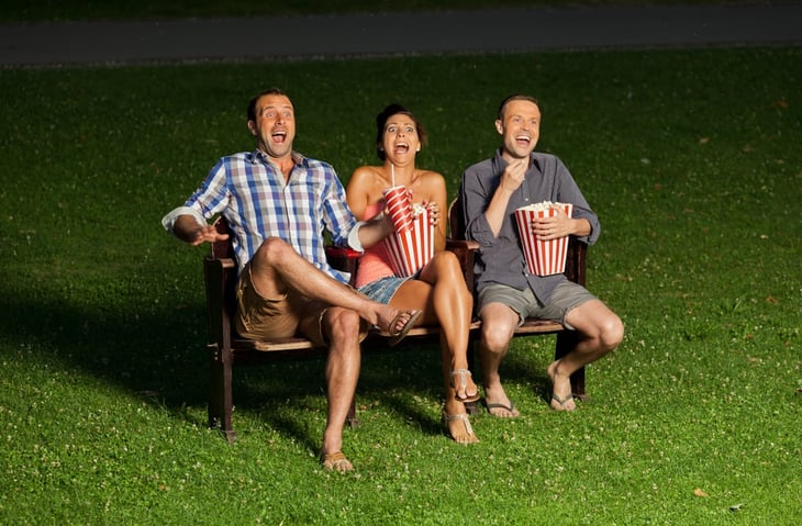 Three adults on a bench eating popcorn