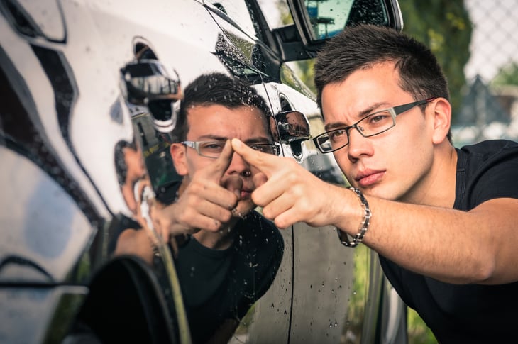 A man inspects a car door for damage