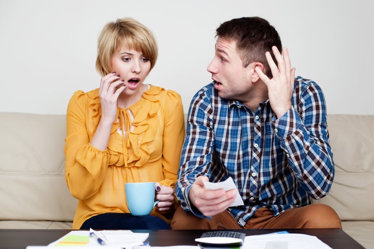 Couple looking at bills, appearing shocked.