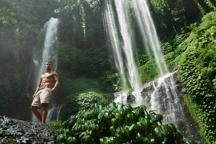 Picture of shirtless man in front of waterfall.