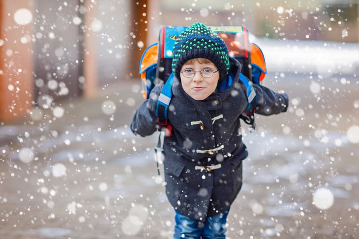Schoolboy with backpack in snow.