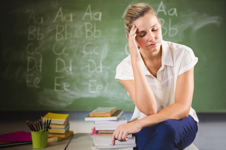 Tired looking teacher sitting in front of chalkboard