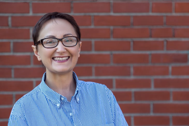 Older woman smiling, brick wall in background.