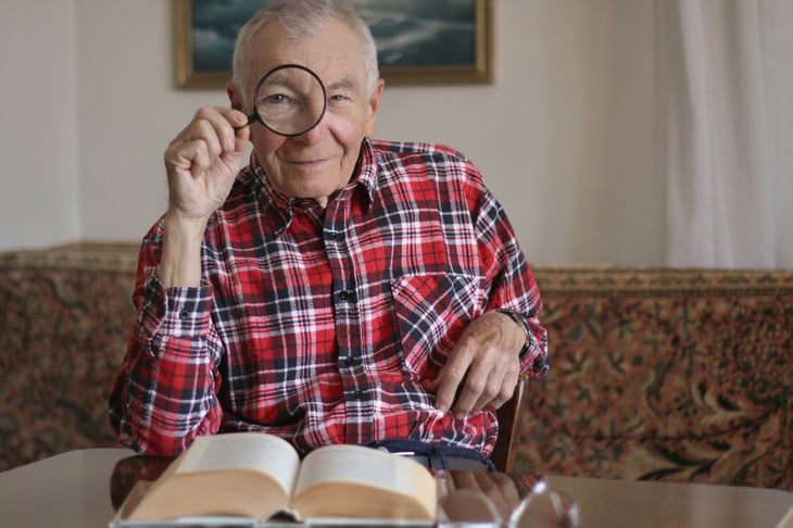 Older man looking through a magnifying glass at the camera
