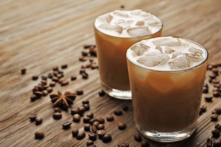 Two cups of iced coffee, with coffee beans scattered on counter.