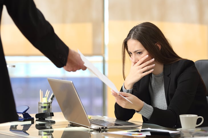 Woman in office receives document, looks shocked.
