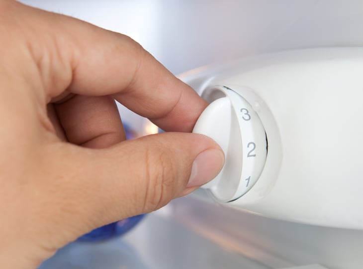 Hand adjusting thermostate in fridge.