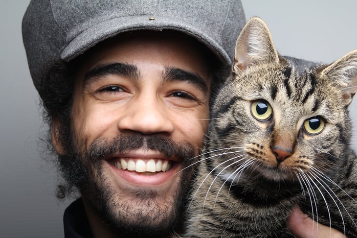 Man's smiling face with grey tabby cat face.