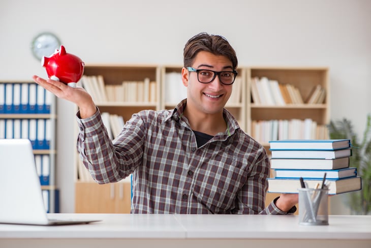 Male student with textbooks in one hand, a piggybank in the other.