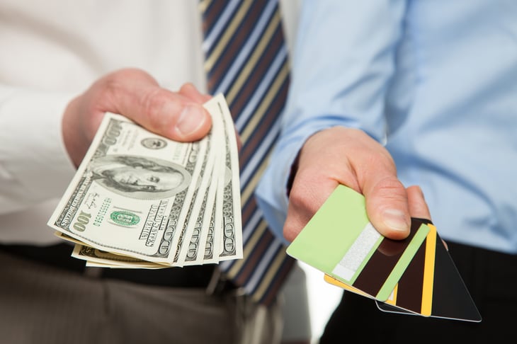 Men in business attire holding out cash and credit cards.