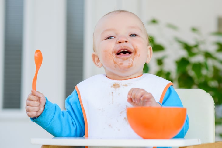Baby eating from a bowl and smiling