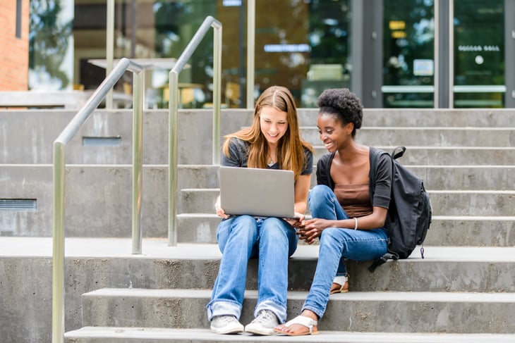 Female students looking at computer on outside stairs.