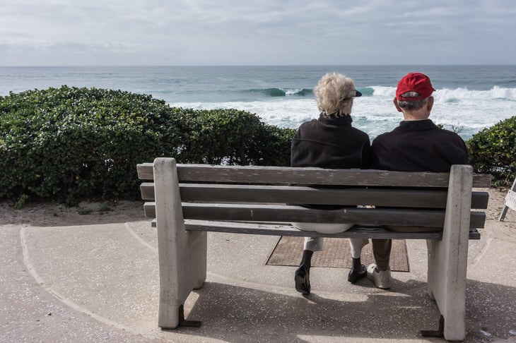 Older couple sitting on a bench overlooking the ocean.