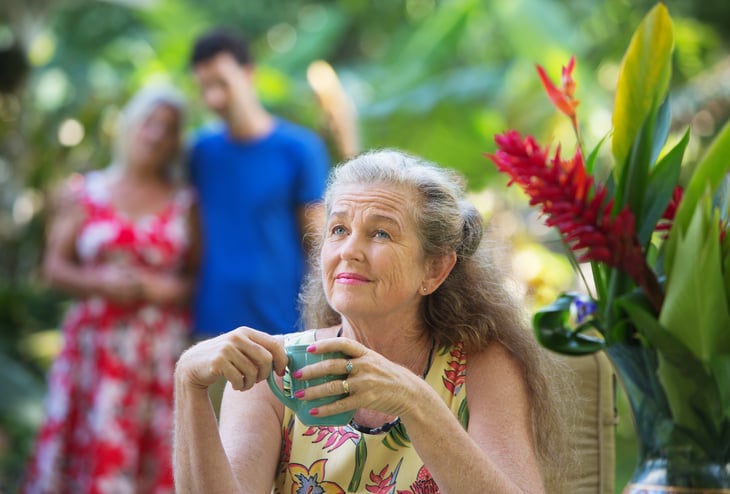 Older woman with cup of coffee in tropical setting.