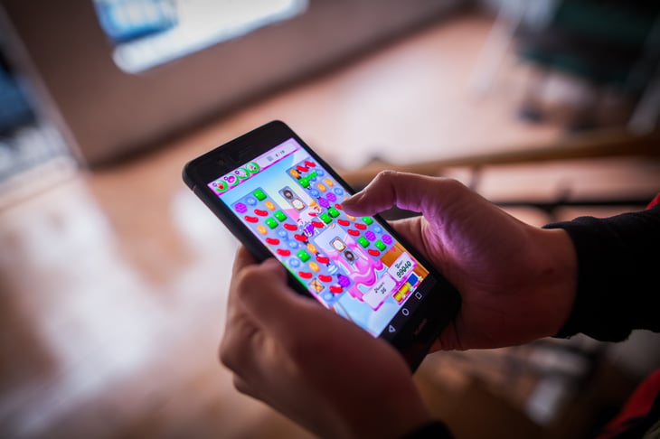 Hands holding cellphone with Candy Crush on it.