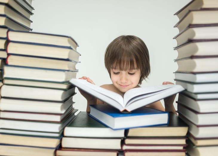 Young boy reading, with books stacked around him