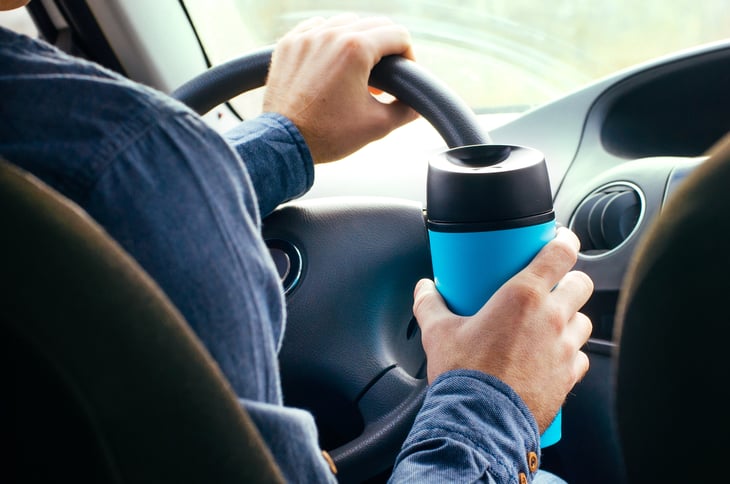 Man with a reusable coffee mug driving
