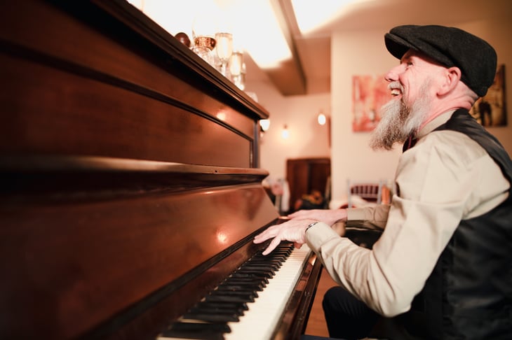 A bearded senior in a hat sings and plays piano music