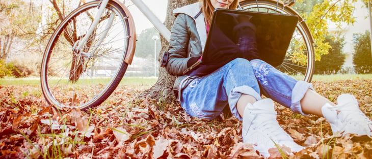 A worker sitting outside in fallen leaves on a laptop