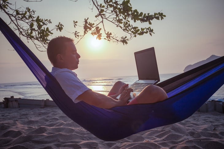 Man on hammock on beach using laptop