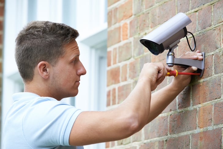 Man installs a security camera on an outdoor wall