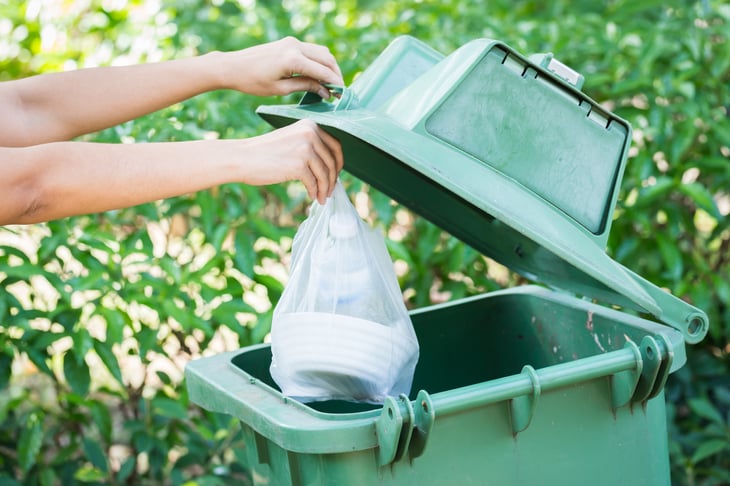 A person puts trash in a trash can outside