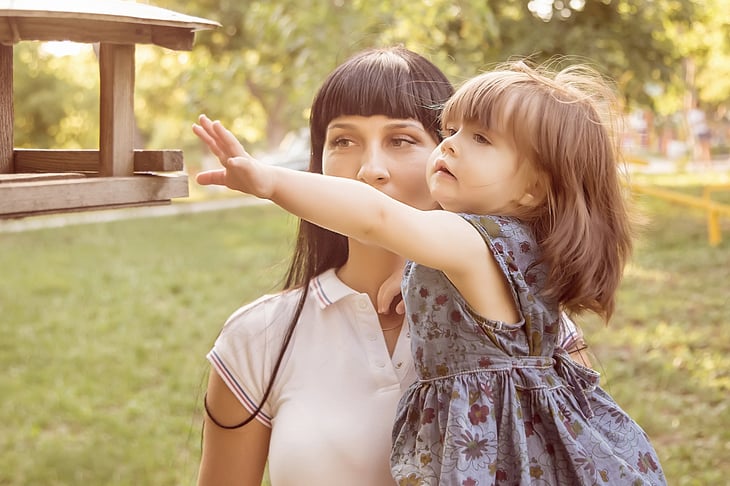 A mother and daughter look at a bird feeder in their yard