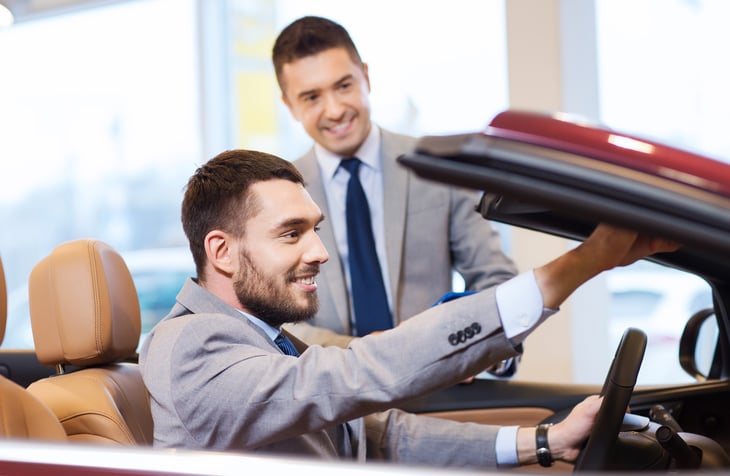 A car shopper looks at a convertible in an auto dealership showroom with a salesman