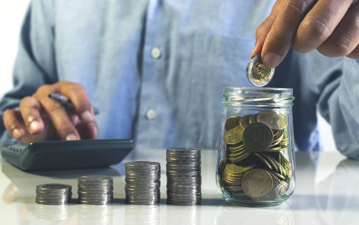man putting coins in glass bottle saving bank