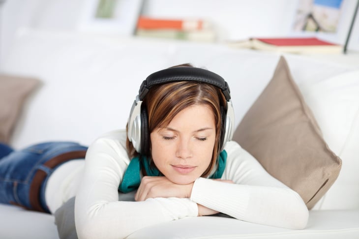 Blissful woman enjoying music on her headphones lying on her stomach on the sofa with her eyes closed in enjoyment