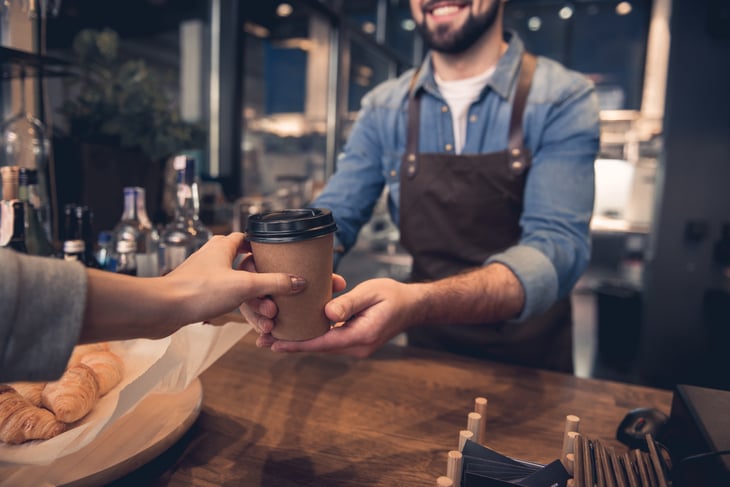 A barista hands a coffee order to a customer