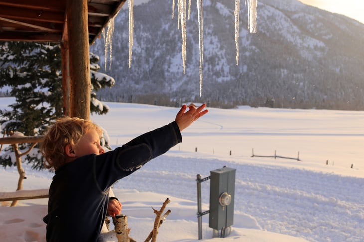 Boy reaching for an icicle, on a cabin porch in Utah mountains