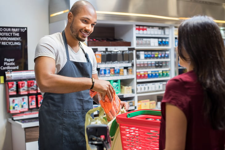 A young black store employee packs a bag of groceries at checkout