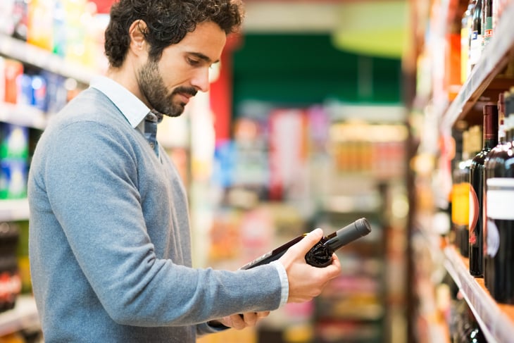 Man reading a wine bottle label at a grocery store