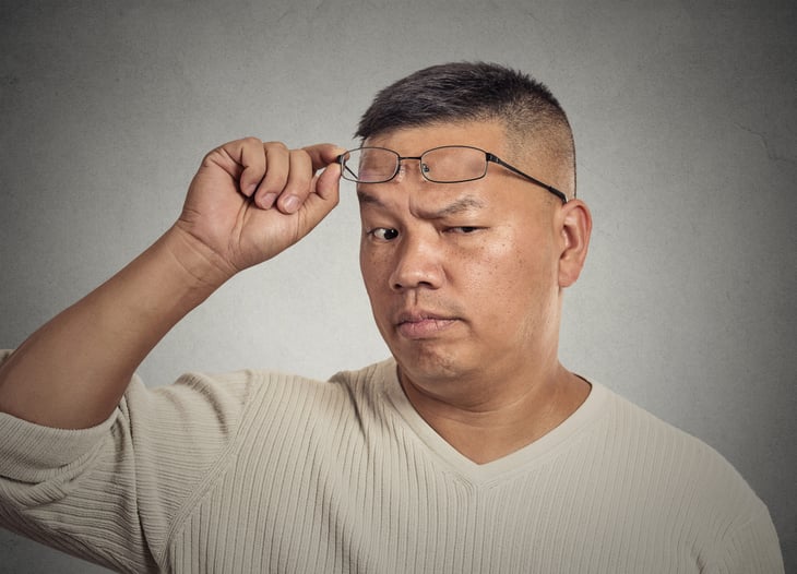 Skeptical man raising his glasses and one eyebrow