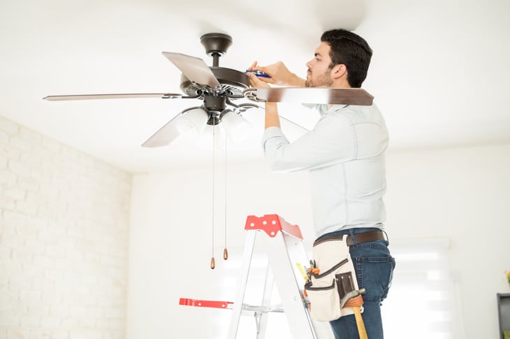 A man adjusts a ceiling fan