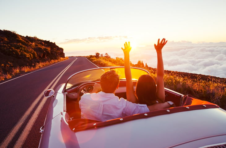 A happy couple drive a convertible car on the highway for a road trip