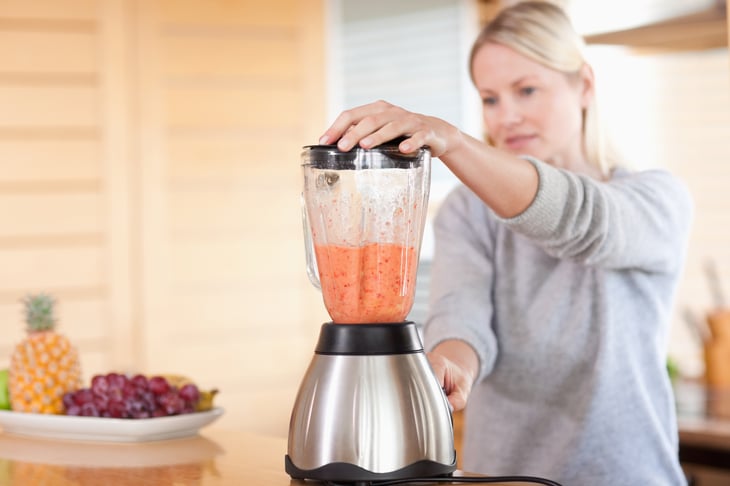 A woman uses a blender to puree fruit in her kitchen