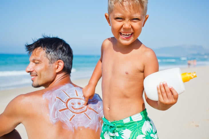 Boy puts sunscreen on dad