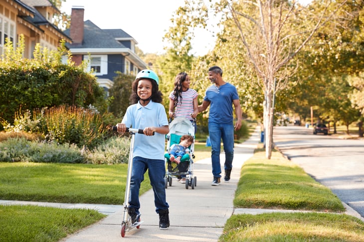 Couple Push Daughter In Stroller As Son Rides Scooter black african american family neighborhood