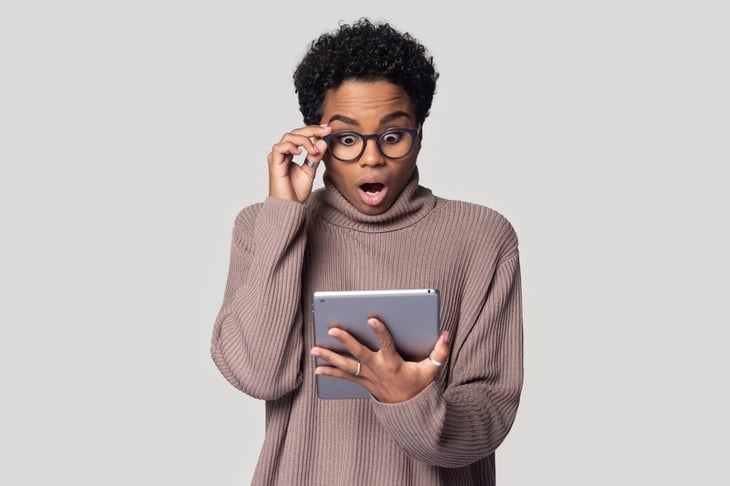 A young black woman in glasses is surprised by something on her tablet computer