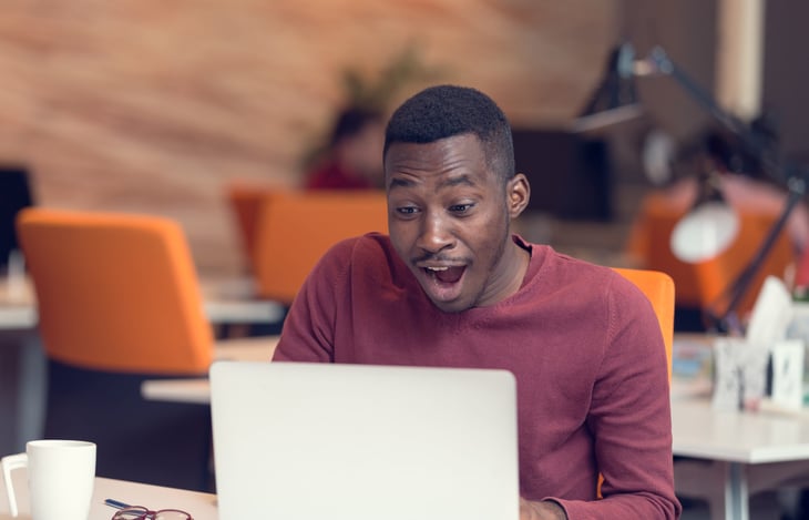 A happy worker is surprised at his desk while on a laptop computer