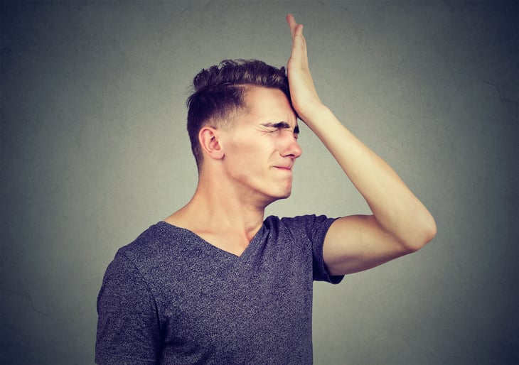 A young man slaps his head and cringes with regret over a stupid mistake