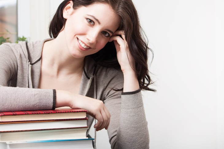 A college student leans on a stack of books