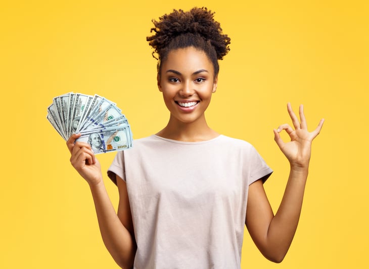woman smiles while holding cash in one hand and gesturing the OK sign with the other hand