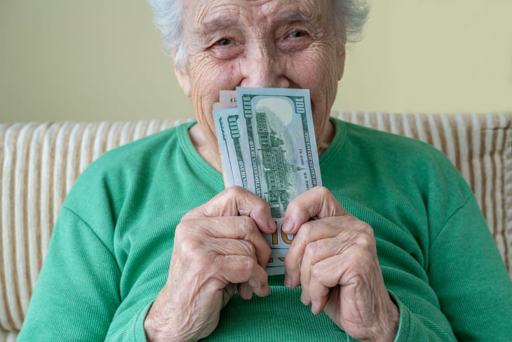 A happy senior holds $100 banknotes