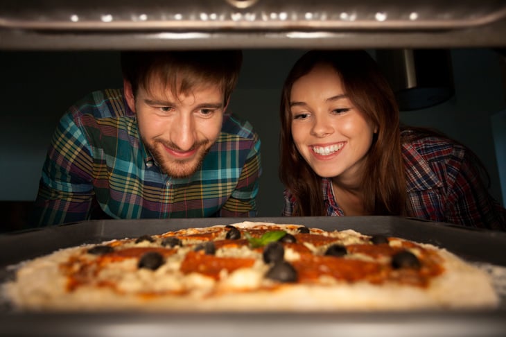 A couple looks at a pizza baking in the oven