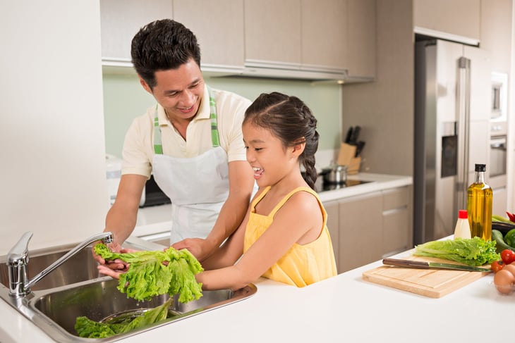 A man washes lettuce in the kitchen sink with his child