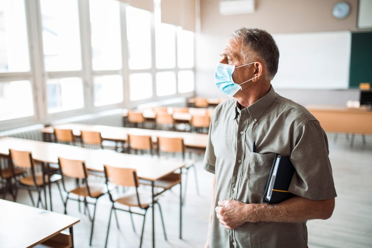 Older teach wearing a face mask in an empty classroom